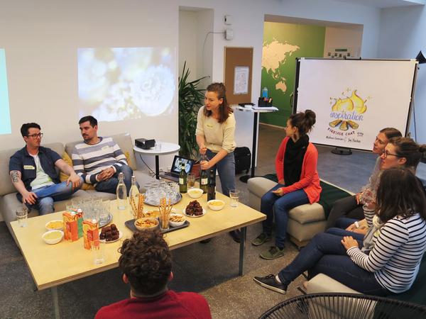 Audience sitting in a circle with drinks and food, graphic recording poster in the background.